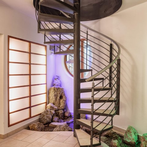 Tageswellness in der Oberpfalz Moderne Wendeltreppe neben dekorativen Steinen und beleuchtetem Wandpaneel