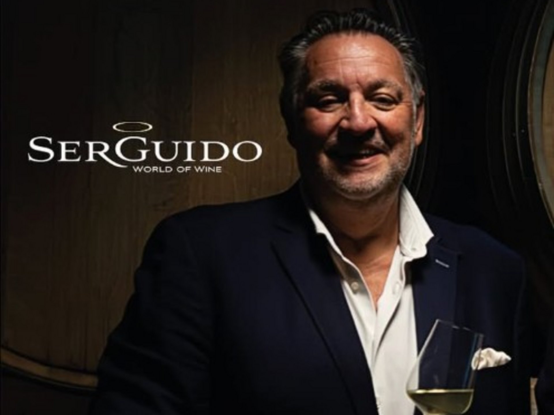 Events & Culinary Experiences in Parsberg Man in suit holding wine glass in front of barrels with Serguido logo