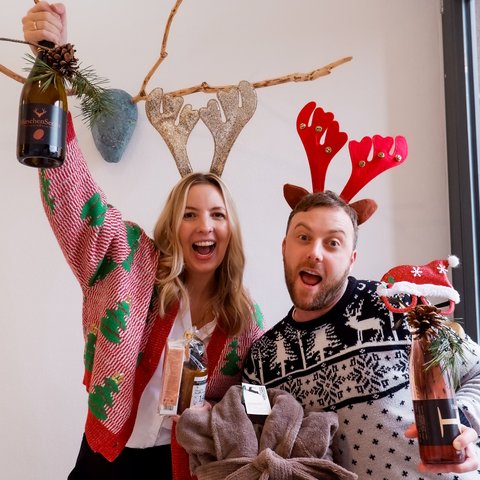 Eco-friendly hotel in Germany with Hirschenmanufaktur Happy couple wearing reindeer antlers and Christmas sweaters holding gifts and drinks