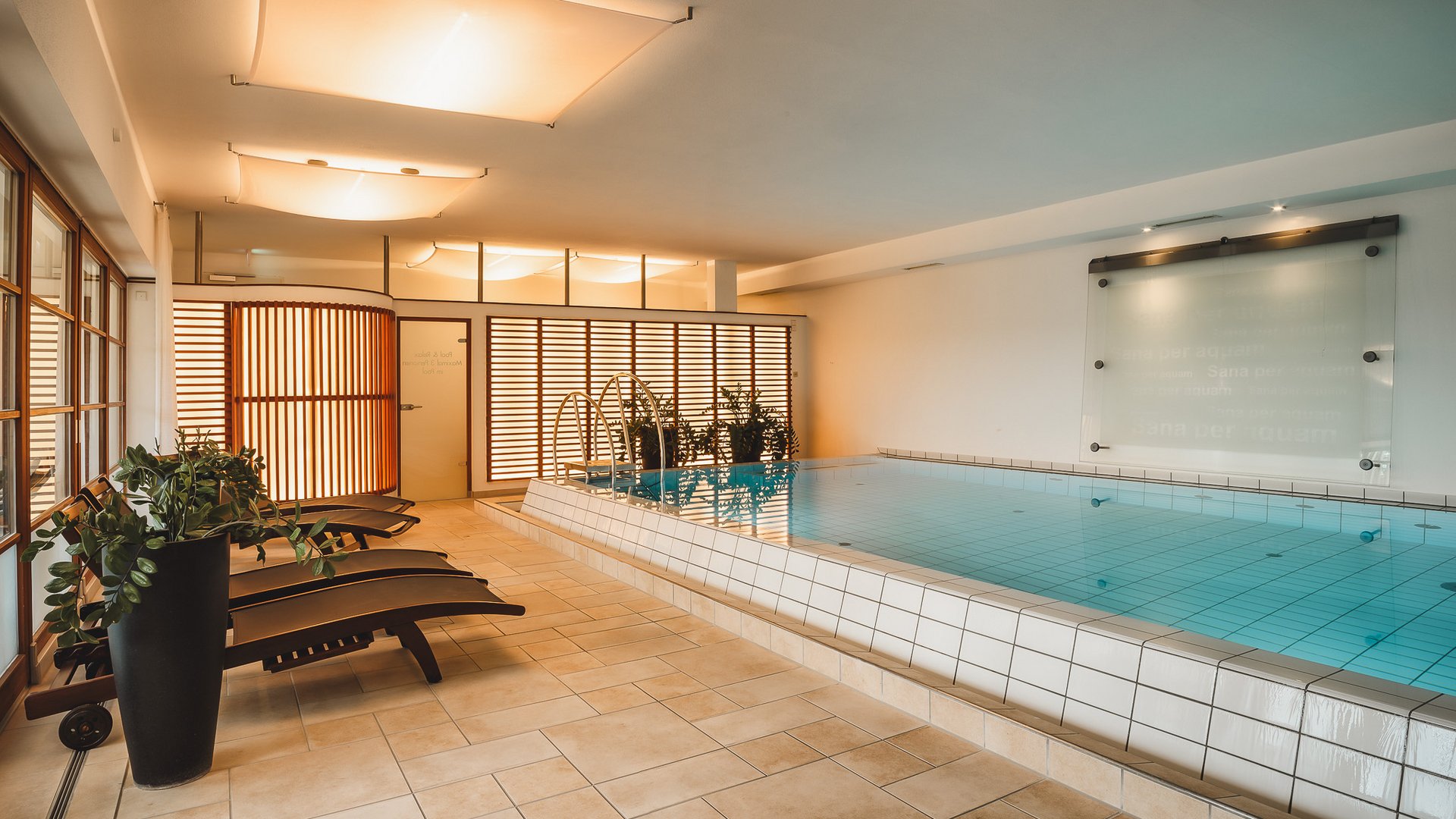 Wellness Indoor pool with lounge chairs and plants in a modern spa area
