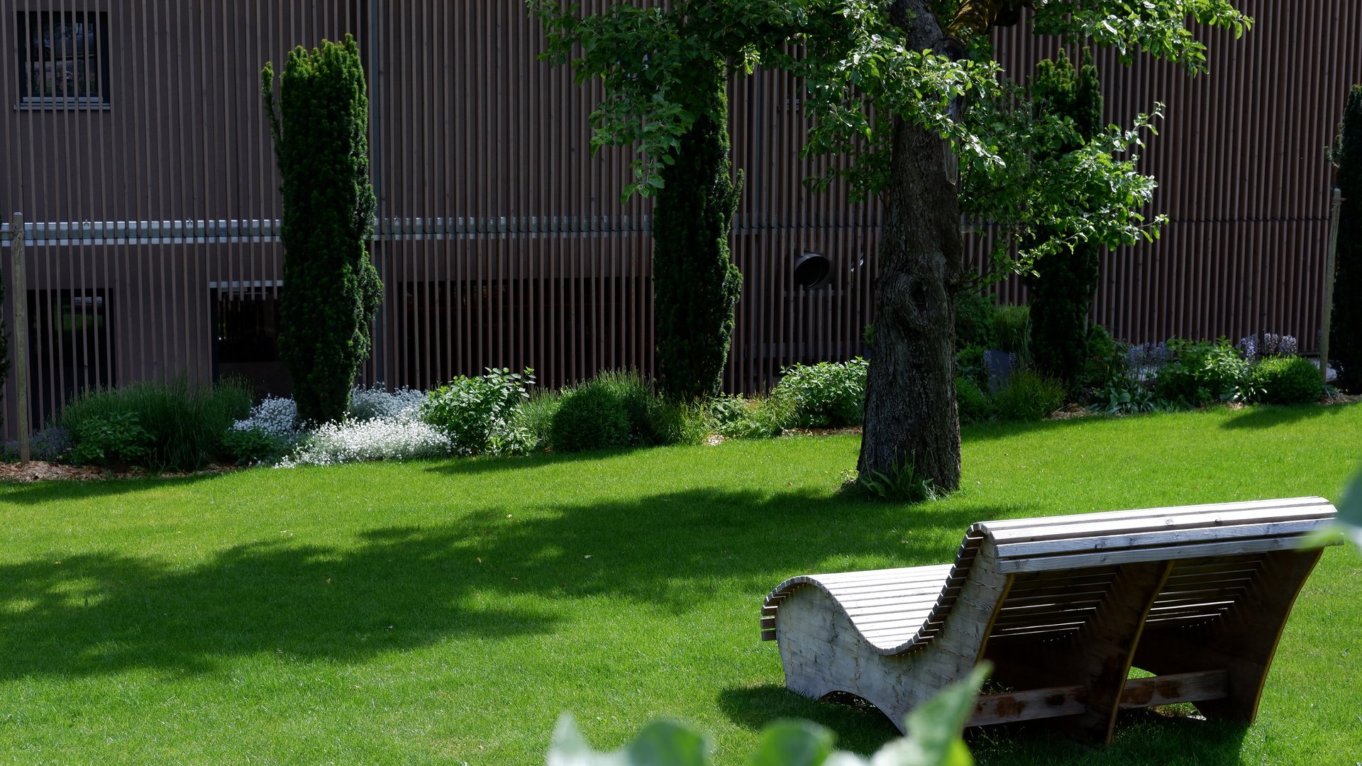 Entspannung in der Oberpfalz: Garten & Ruheräume Grüne Wiese mit moderner Holzliege und Bäumen im Hintergrund
