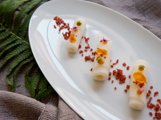 Romantik Hotel Hirschen: Bildergalerie Drei gerollte feine Vorspeisen auf weißem Teller mit bunten Blüten und Gewürzen