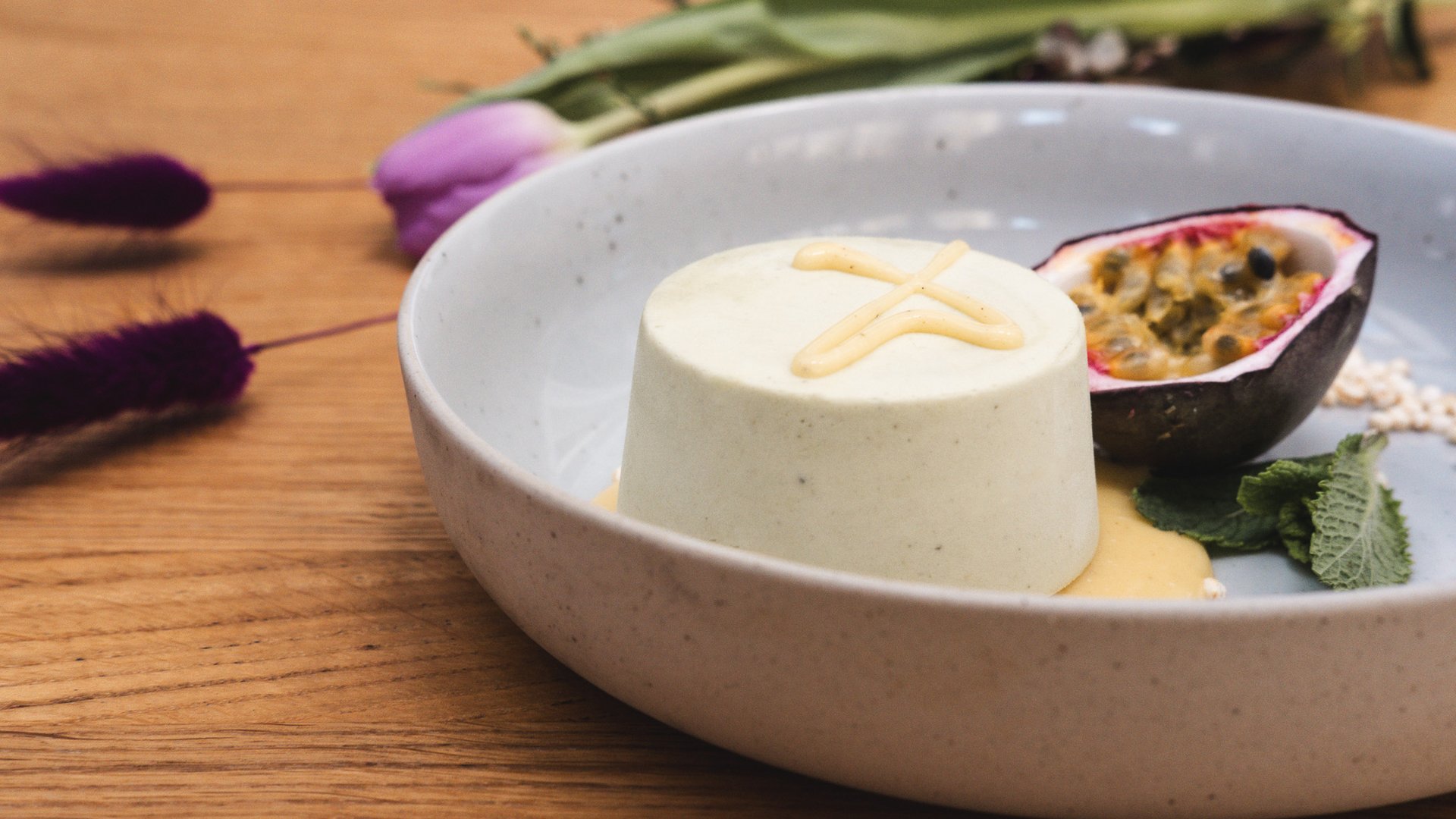 Romantik Hotel Hirschen: Kulinarik Vanillepanna cotta mit Passionsfrucht und Minze auf weißem Teller