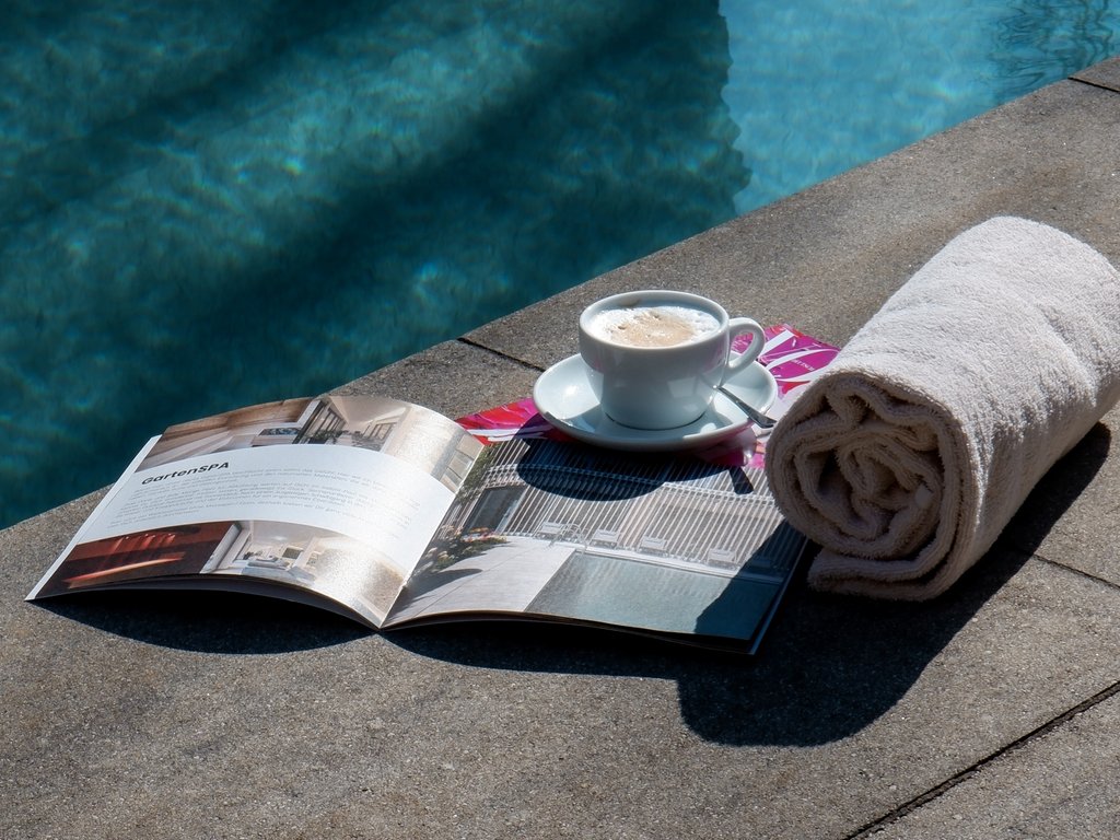 Wellnesshotel Parsberg – Romantik Hotel Hirschen Kaffeetasse, Handtücher und Magazin am Poolrand