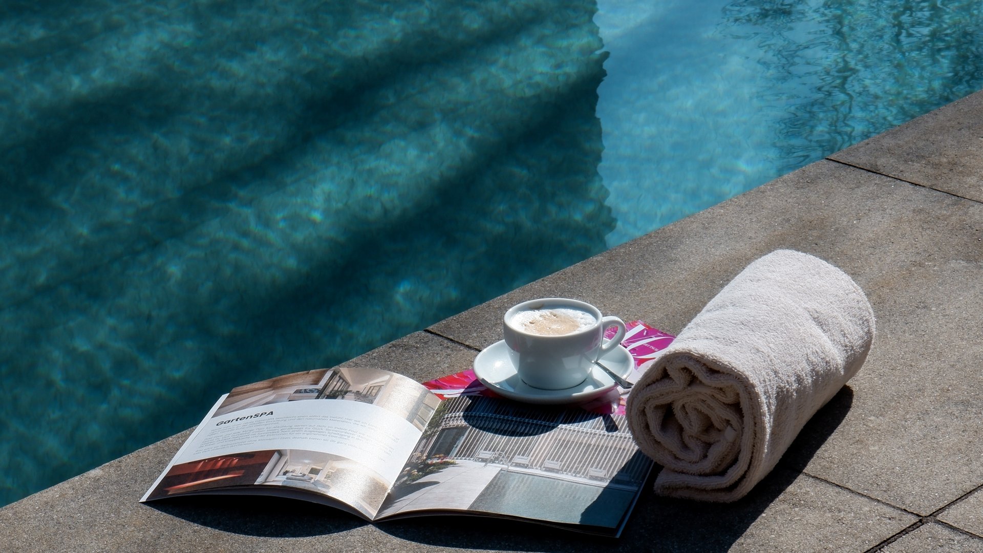 Workation Kaffeetasse, Handtücher und Magazin am Poolrand