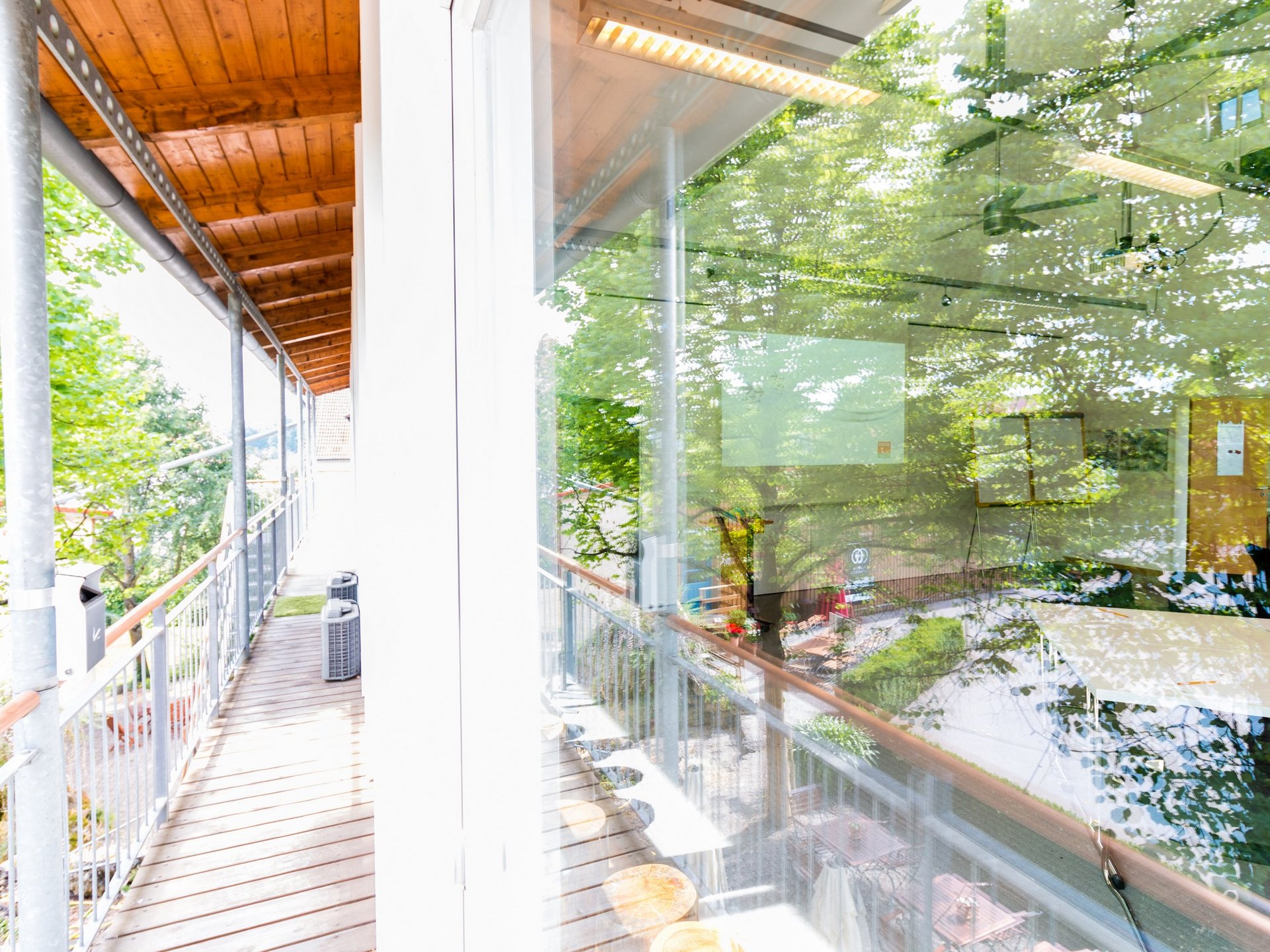 Tagungsräume mit moderner Technik in der Oberpfalz Flur mit Holzgeländer und reflektierenden Fenstern neben grünen Bäumen
