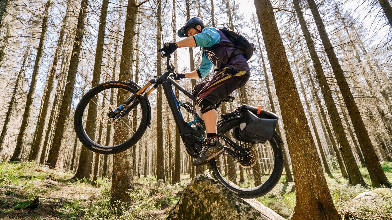 Mountainbiker springt mit E-Bike über Felsen im Wald
