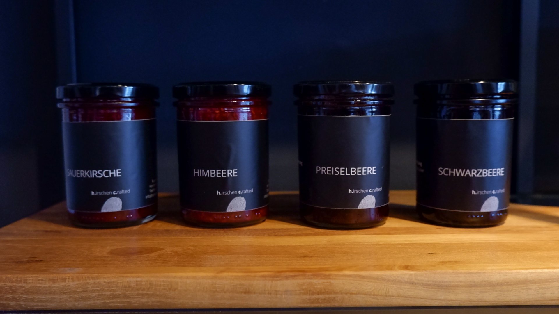 Nachhaltige Hotels in Deutschland gesucht? Vier Gläser mit verschiedenen Fruchtaufstrichen auf Holzbrett