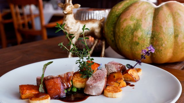 Romantik Hotel Hirschen: Blog Fein angerichtetes Gericht mit Fleisch, Gemüse und Kräutern vor Kürbis und Hirschfigur