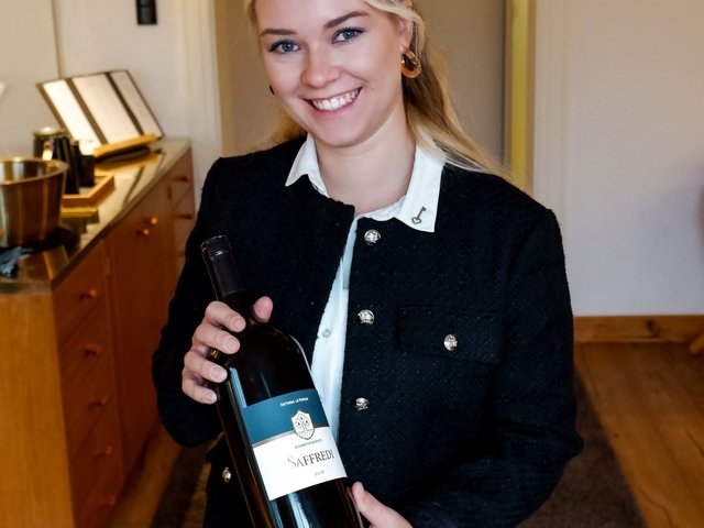 Romantik Hotel Hirschen: Bildergalerie Frau hält eine Flasche Saffredi Rotwein lächelnd in Innenraum