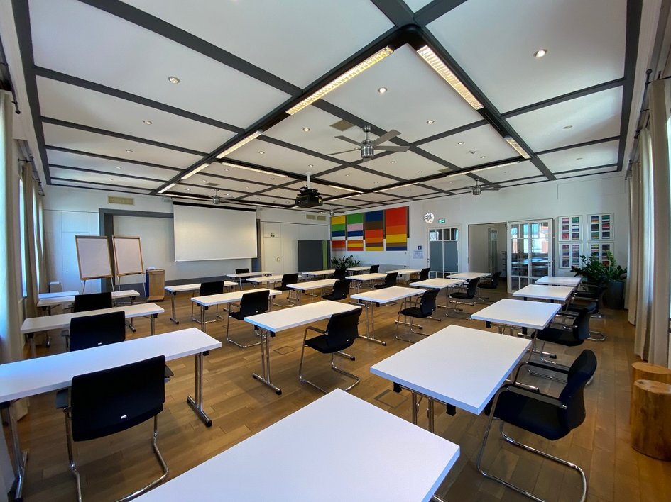 Looking for somewhere for conferences in Bavaria? Empty bright seminar room with tables, chairs, and projection screen