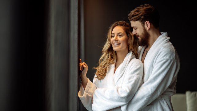 Wellness in der Oberpfalz: Massage & Beauty Paar im weißen Bademantel, steht lächelnd am Fenster