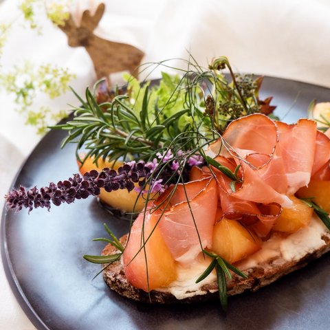 Kulinarik & Genuss in der Oberpfalz Brot mit Schinken, Melone und frischen Kräutern auf einem schwarzen Teller