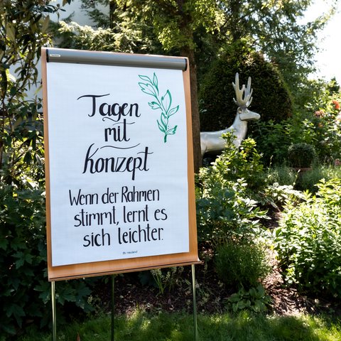 Tagungshotel Oberpfalz: Das Hotel für Deine Tagung Flipchart mit handgeschriebenem Spruch in einem Garten mit Skulptur