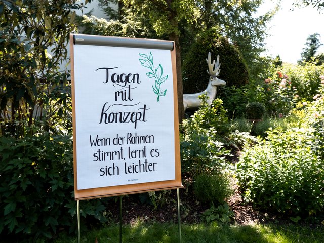 Romantik Hotel Hirschen: Bildergalerie Flipchart mit handgeschriebenem Spruch in einem Garten mit Skulptur