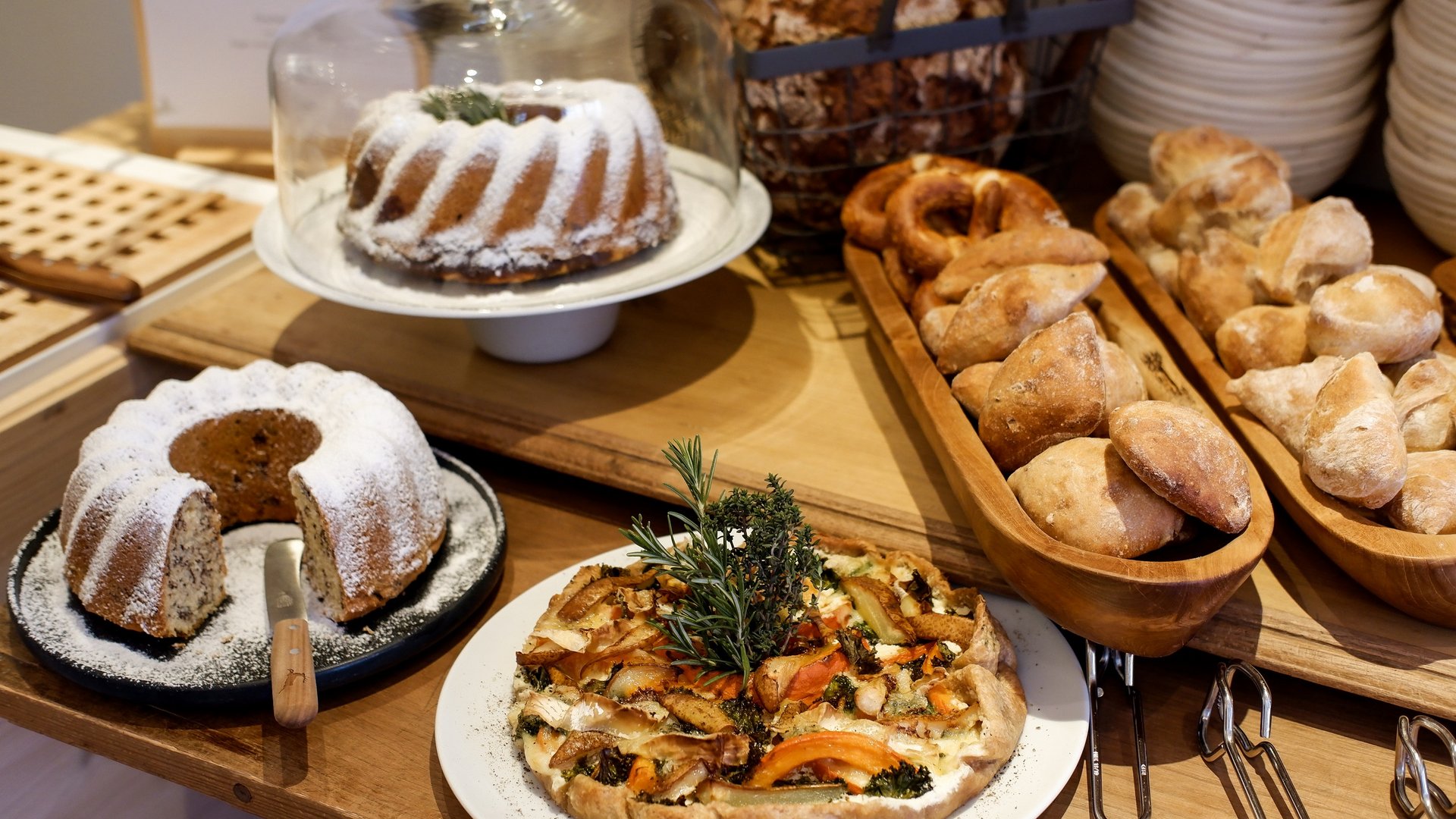 Romantik Hotel Hirschen: Frühstück Verschiedene Backwaren wie Gugelhupf, Brot, Brezeln und Gemüsetarte auf Holztisch