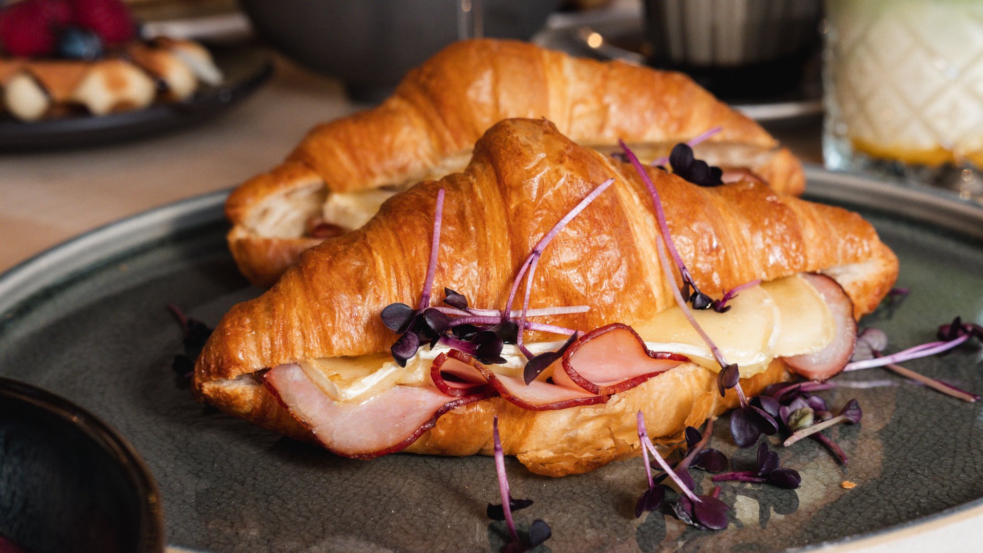 Brunch – breakfast for late risers Two croissant sandwiches with ham, cheese, and fresh herbs on a plate