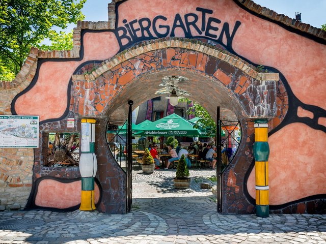 Romantik Hotel Hirschen: Bildergalerie Eingang zum Biergarten mit bunter Mauer und Gästen an Tischen im Schatten