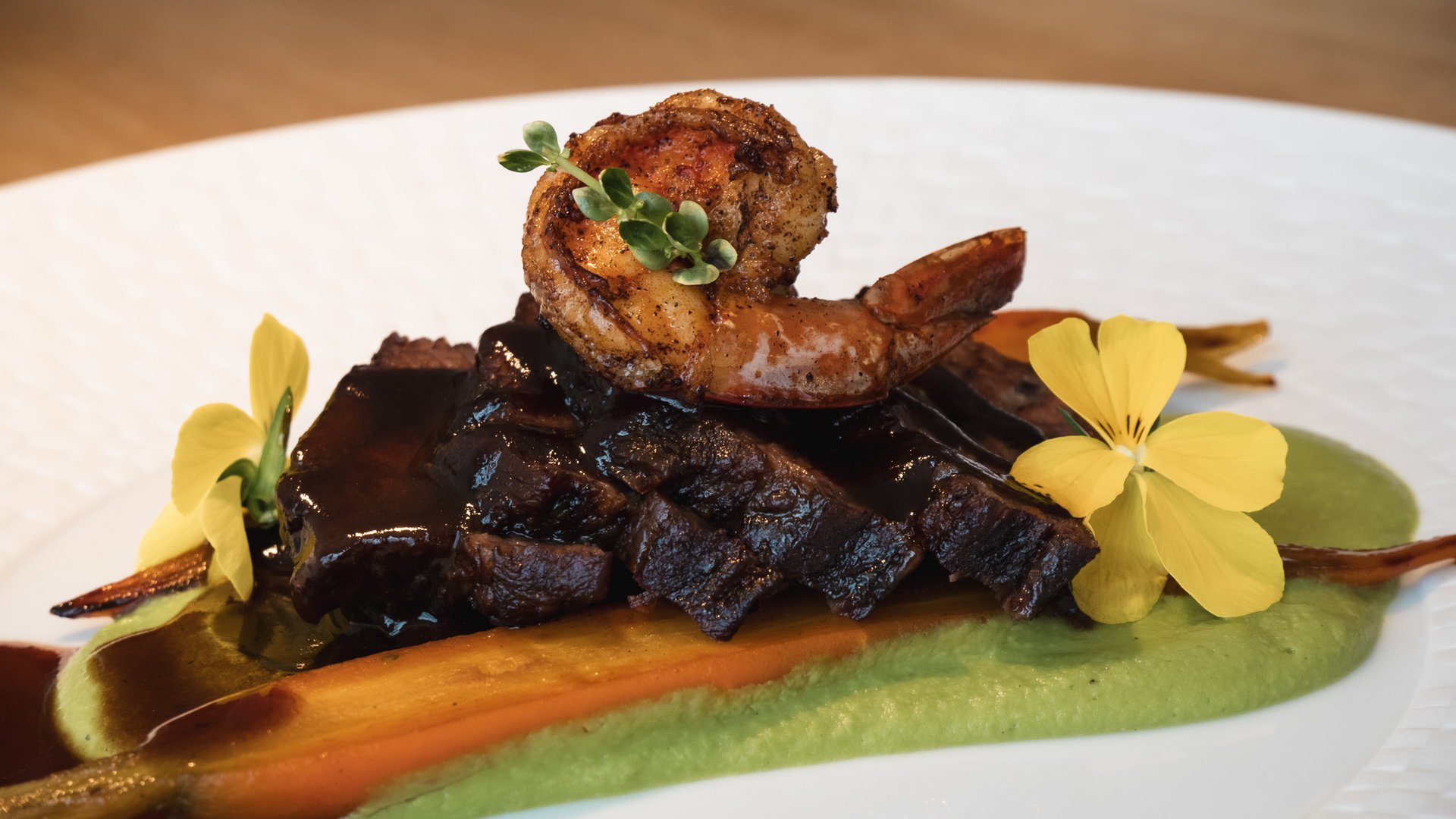 Home Gourmet dish with grilled shrimp, meat, carrot, and flowers on green puree