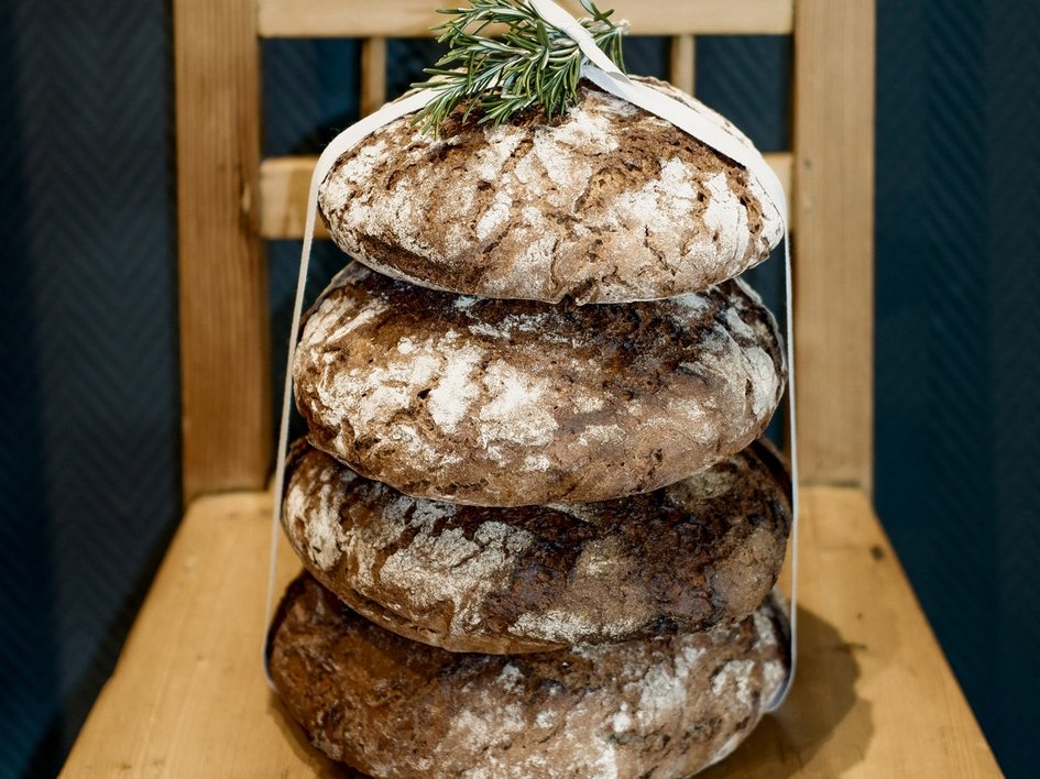 Nachhaltiges Hotel in Bayern mit Hirschenmanufaktur Vier runde Brote mit Mehl bestäubt, gestapelt auf einem Holzstuhl