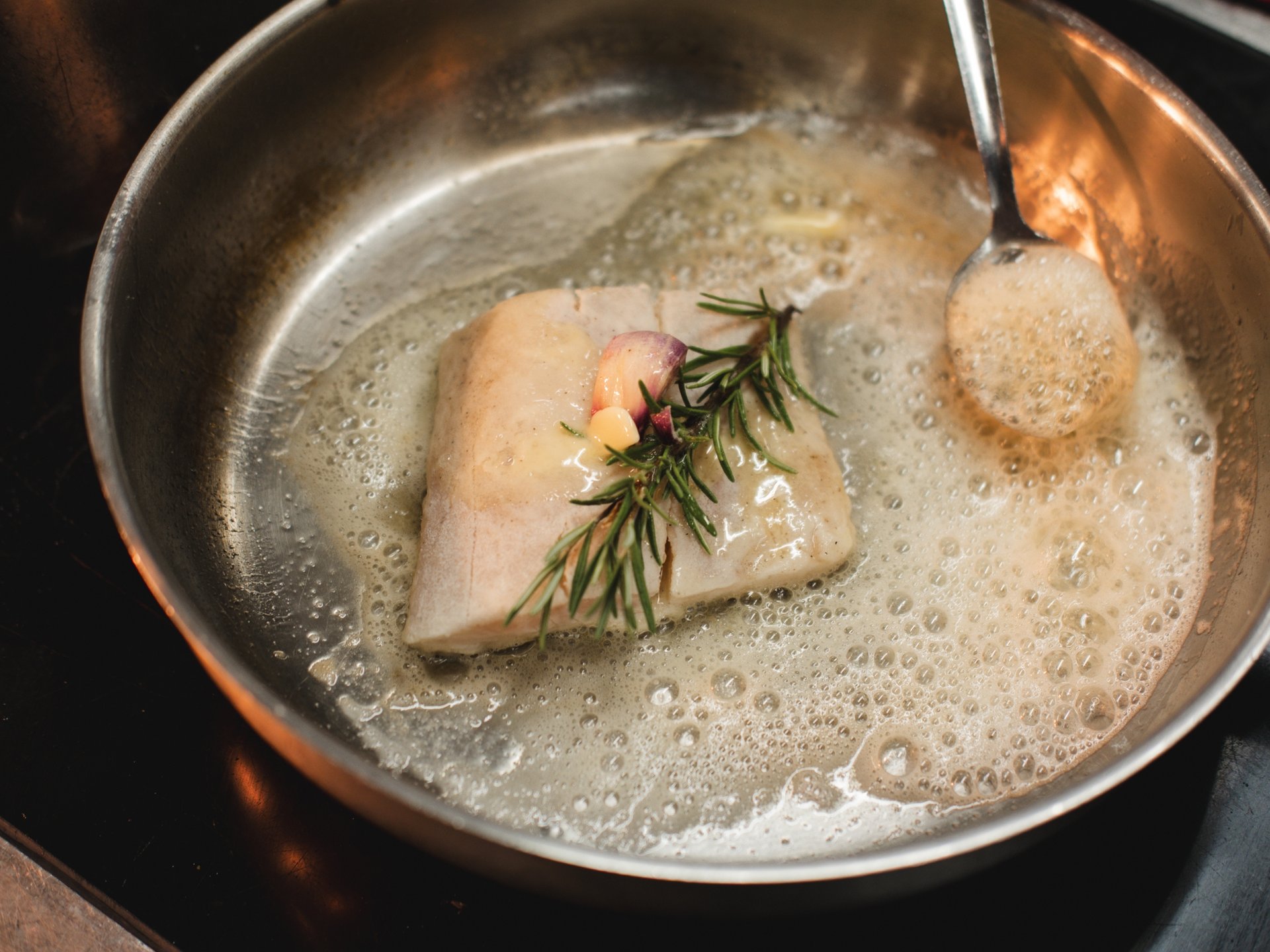 Nachhaltigkeit aus Überzeugung. Fischfilet mit Knoblauch und Rosmarin in einer Pfanne mit Butter gebraten