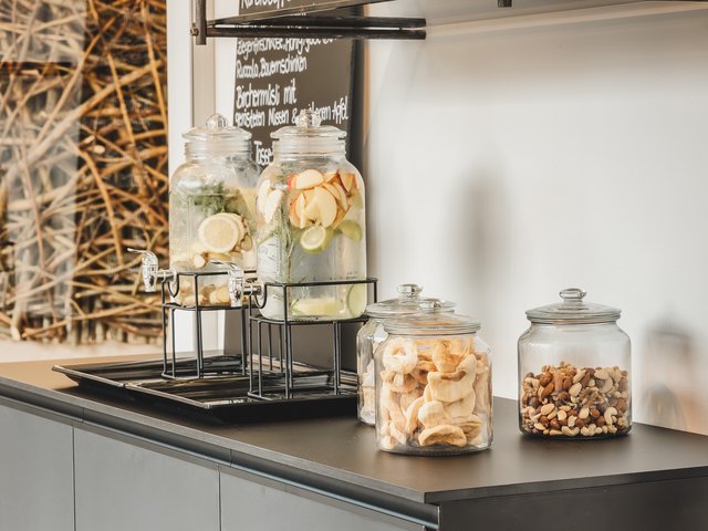 Romantik Hotel Hirschen: Bildergalerie Wasserspender mit Früchten und Gläser mit Nüssen und getrocknetem Obst auf schwarzer Theke