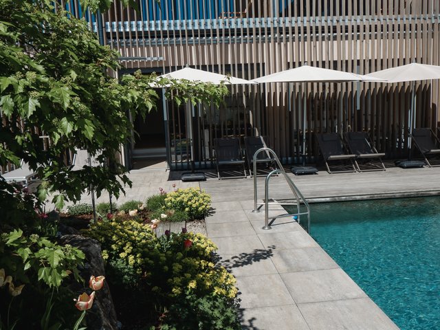 Romantik Hotel Hirschen: Bildergalerie Pool mit Liegestühlen und weißen Sonnenschirmen neben einem Blumenbeet