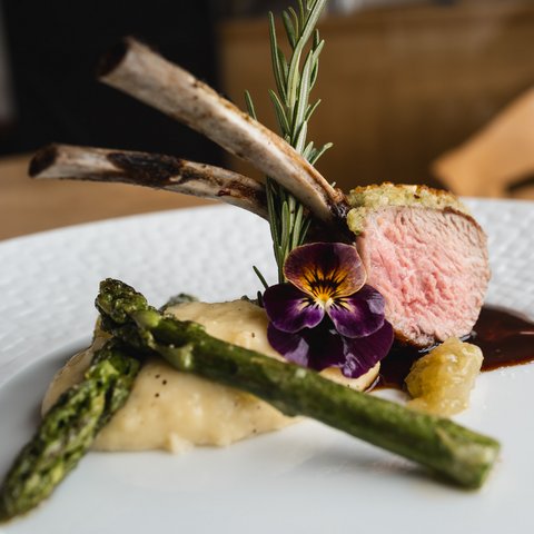 Kulinarik & Genuss in der Oberpfalz Lammkotelett mit Kräutern, Spargel und Blume auf einem weißen Teller