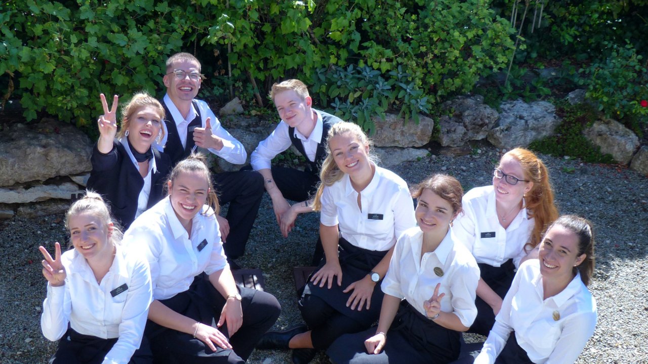 Gruppe junger Kellner im Arbeitsoutfit sitzt im Garten und lächelt in die Kamera