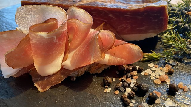 Gasthof Parsberg: Ein Gruß an den guten Geschmack Aufgeschnittene luftgetrocknete Speckscheiben mit Gewürzen und Kräutern auf schwarzem Stein