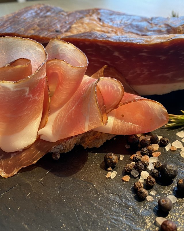 Guesthouse in Parsberg: A salute to great taste Sliced cured speck with spices and herbs on a black stone slab
