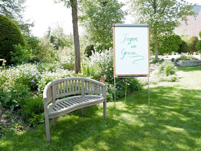 Romantik Hotel Hirschen: Bildergalerie Gartenbank und Flipchart mit Schriftzug Tagen im Grünen in blumigem Garten