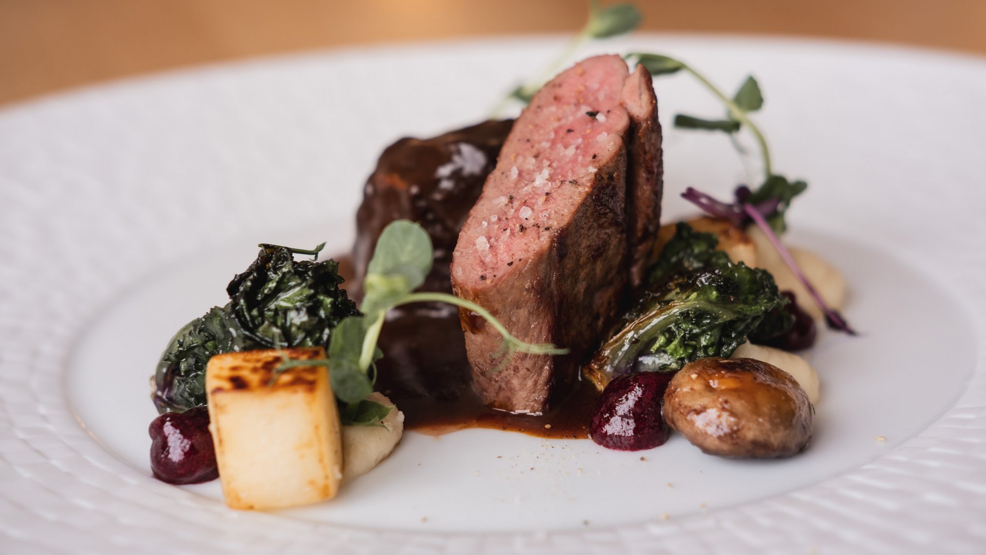 Hotel mit frühem Check-in Gourmetgericht mit rosa gebratenem Fleisch, Pilzen und Gemüse auf weißem Teller