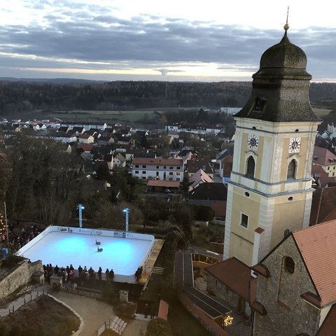 Hotels in Regensburg und Umgebung: kultur-trächtig! Eislaufplatz mit Beleuchtung neben historischem Kirchturm in einem Dorf bei Dämmerung