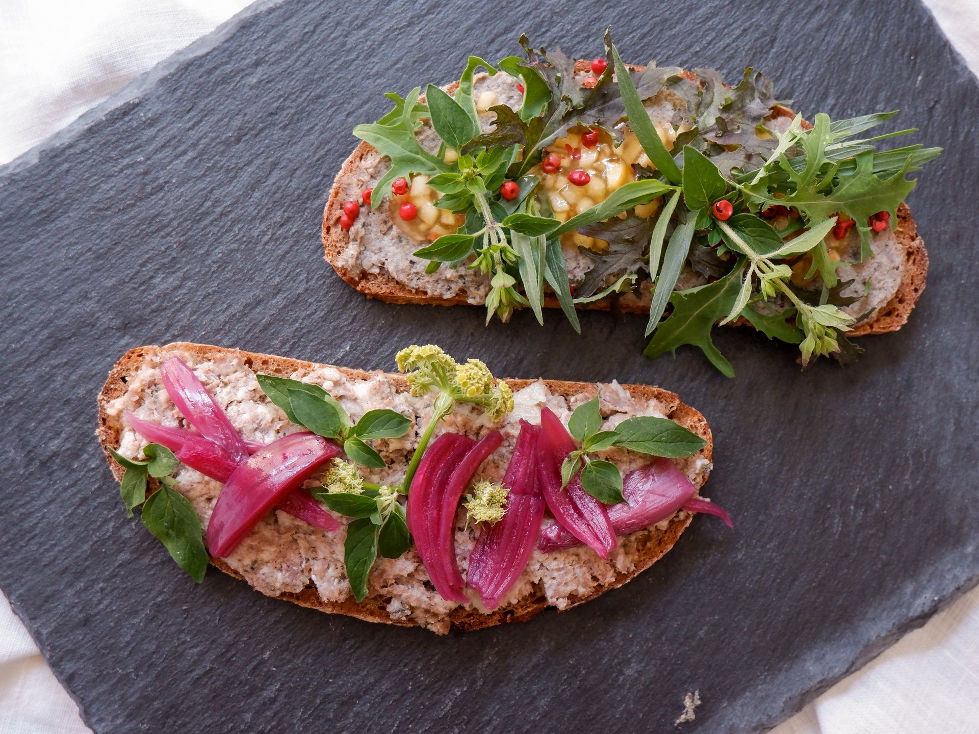 Tagungspauschalen, Räume & Preise für Seminare und Tagungen Zwei belegte Brotscheiben mit Frischkäse, roten Zwiebeln und frischen Kräutern auf Schieferplatte