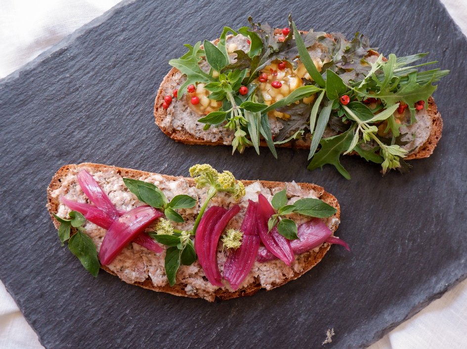 Leistungen und Preise für Tagungen und Konferenzen Zwei belegte Brotscheiben mit Frischkäse, roten Zwiebeln und frischen Kräutern auf Schieferplatte