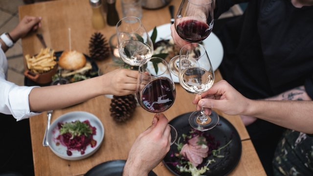 Geschichten aus dem Hirschen und der Oberpfalz. Vier Personen stoßen mit Rot- und Weißwein über einem gedeckten Esstisch an