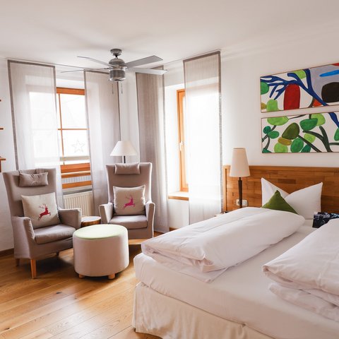 Romantik Hotel Hirschen: Gastgeber & Werte Gemütliches Schlafzimmer mit Doppelbett, zwei Sesseln und bunter Wandkunst
