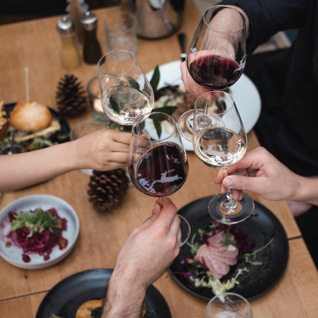 Home Menschen stoßen mit Rot- und Weißweingläsern über einem gedeckten Tisch an