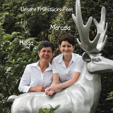 Romantik Hotel Hirschen: Frühstück Zwei Frauen in weißen Hemden sitzen an einer silbernen Hirschfigur im Garten