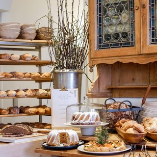 Romantik Hotel Hirschen: Gastgeber & Werte Bäckerei mit verschiedenen Broten, Kuchen und Holzregalen mit Tellern