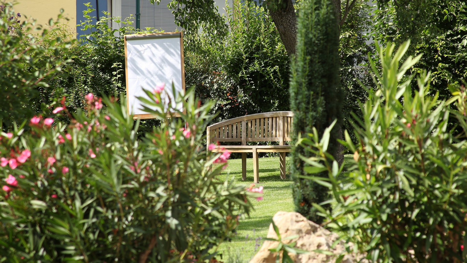 Tagungshotel mit Events gesucht? Holzbank und leeres Flipchart in einem grünen Garten mit blühenden Sträuchern