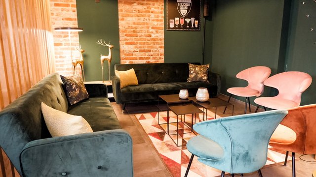 Romantik Hotel Hirschen: Blog Gemütliches Wohnzimmer mit grünen Sofas und bunten Stühlen vor Backsteinwand