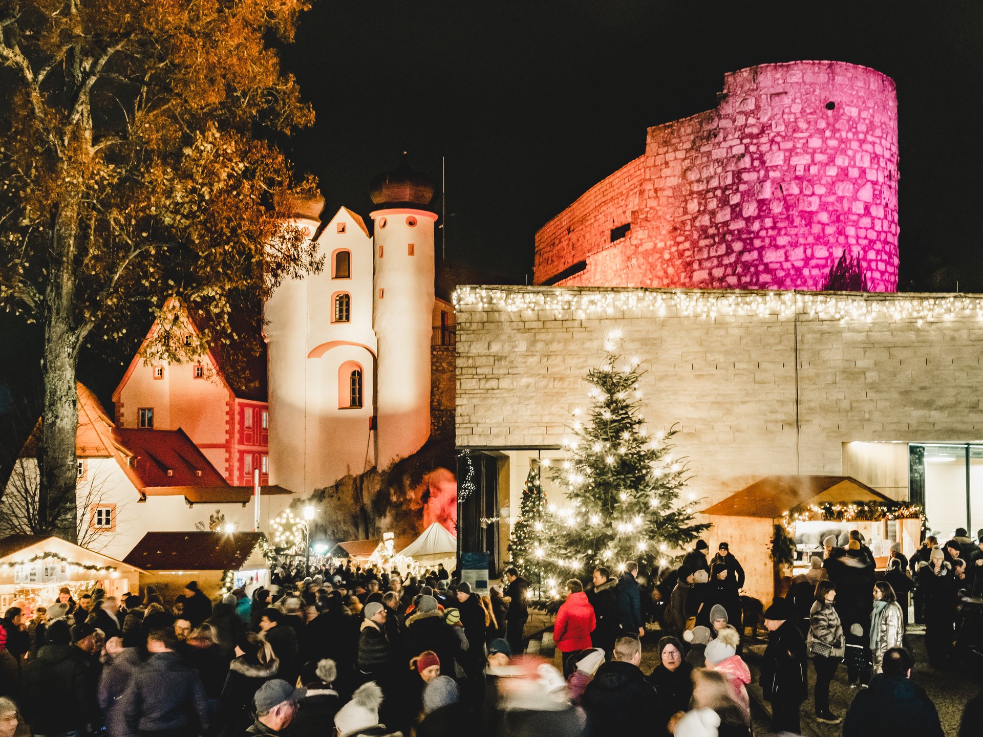 Weihnachtsmärkte Weihnachtsmarkt mit Menschen vor beleuchteten historischen Gebäuden und einem festlich geschmückten Baum