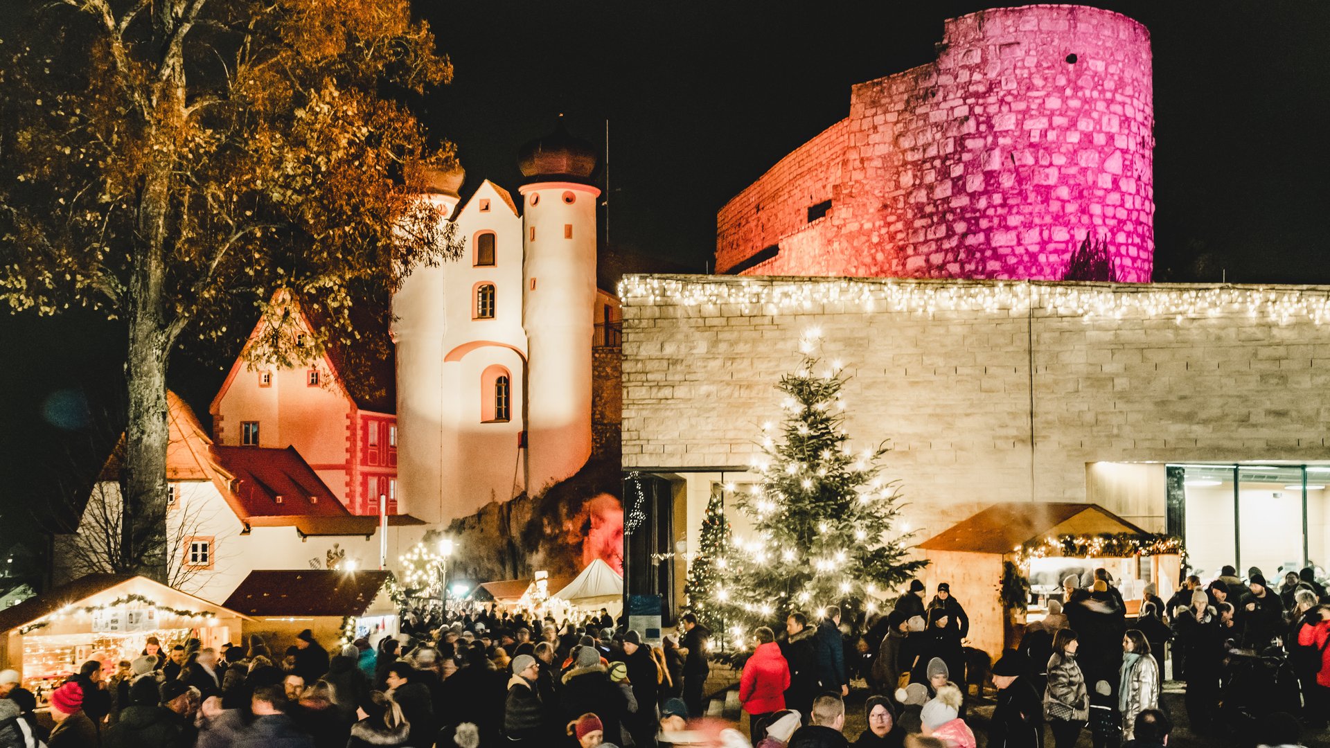 Weihnachtsmärkte Weihnachtsmarkt mit Menschen vor beleuchteten historischen Gebäuden und einem festlich geschmückten Baum