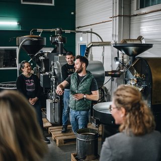 Leistungen und Preise für Tagungen und Konferenzen Gruppe bei einer Führung durch eine Kaffeerösterei mit Maschinen im Hintergrund