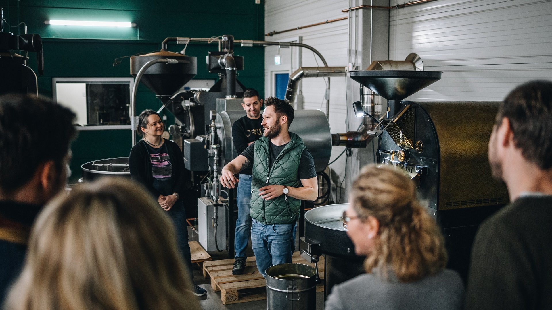 Services and rates for conferences and celebrations Group on a tour inside a coffee roastery with roasting machines in the background