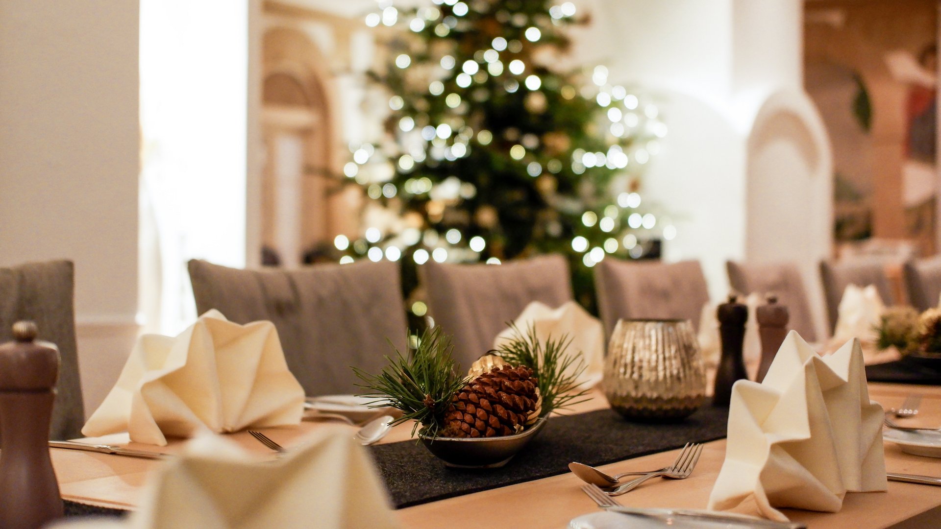 Weihnachtsmenüs 2025 Festlich gedeckter Tisch mit Tannenzapfen und Weihnachtsbaum im Hintergrund