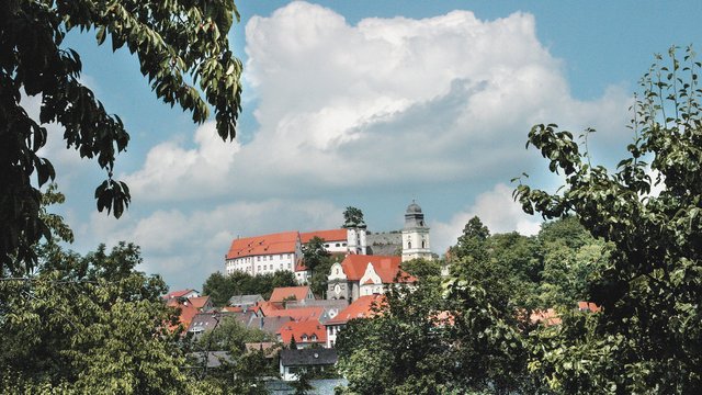 Familienhotel Oberpfalz: Hier gibt’s so viel zu erleben! Blick auf ein Dorf mit roten Dächern und einer Kirche hinter Bäumen bei wolkigem Himmel