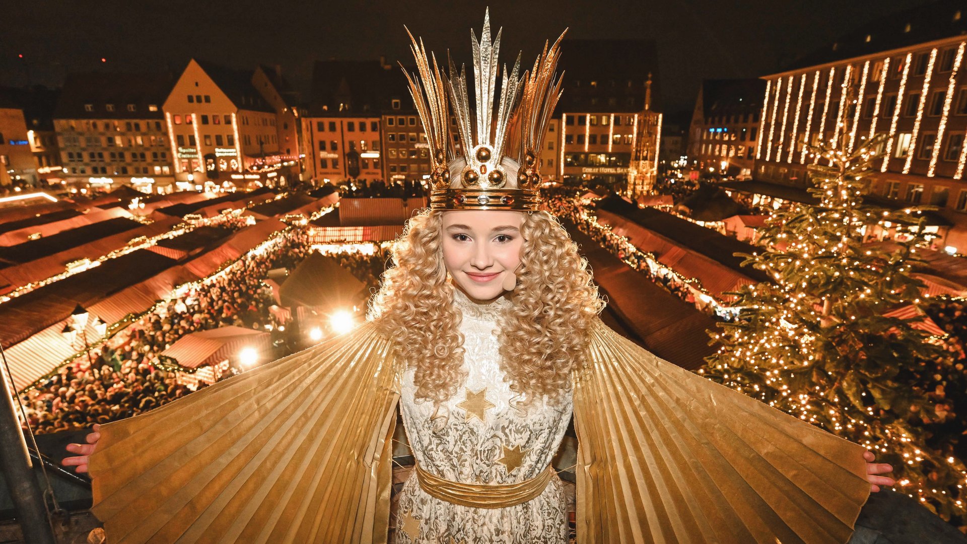 Weihnachtsmärkte Mädchen in festlichem Kleid und Krone vor einem beleuchteten Weihnachtsmarkt bei Nacht